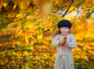 Pretty girl in autumn hat and cardigan posing with leaves in the park. Copy space.