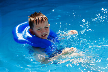 Fototapeta na wymiar Happy kid in vest at swimming pool . Chilhood, leisure, swimming theme. Boy In Life Jacket.