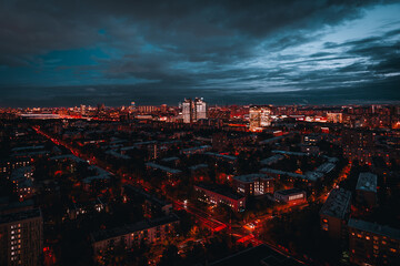 A wide-angle long-exposure aerial view from a drone of a night urban cityscape with deep blue sky,...