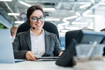 A happy female support operator is sitting at a desk and answering calls. Beautiful smiling woman...