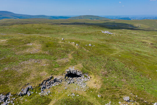 Aerial view of the entrance to an underground cave system on remote moorland (Chartist Cave, Wales, UK)