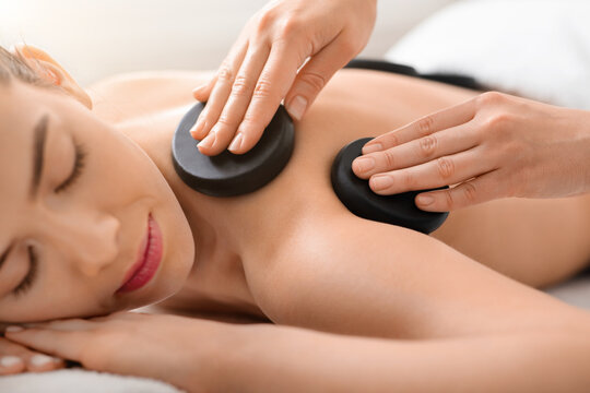Massage therapist putting black stones on woman shoulders