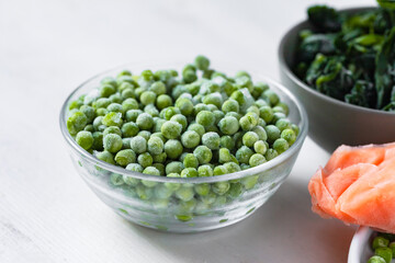 Frozen vegetables and fish: green peas, spinach, salmon. Concept of healthy eating, easy cooking. White background copy space for text. Close up macro