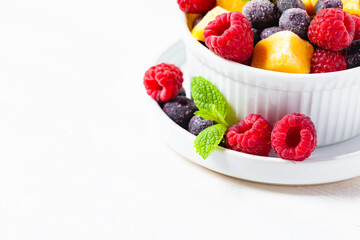 Frozen fruits: mango, raspberry, blueberry with fresh green mint in white bowl. Concept of healthy eating, delicious low calories dessert, summer refreshing light meal. White background copy space