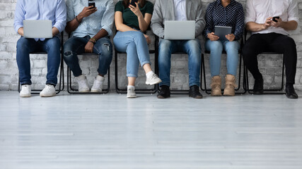 Conceptual photo six multi ethnic young people sit in queue holding electronic devices using internet while waiting job interview. Generation addicted with modern devices, employment, human resources