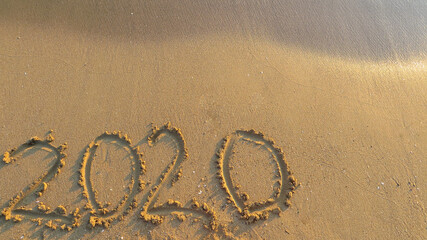 Title 2020 on a sandy beach with a sea wave above. Sea surf. Copyspace.