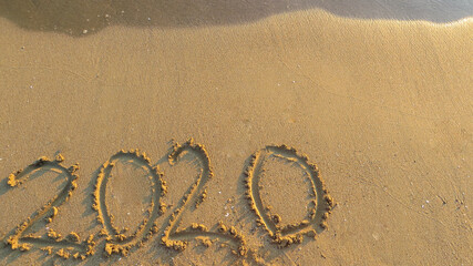 Title 2020 on a sandy beach with a sea wave above. Sea surf. Copyspace.