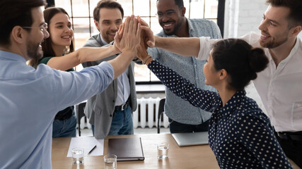 Group of excited multi-ethnic office staff members stack palms together express unity, giving high...
