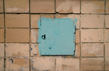 Old metal small door painted with blue paint against the background of an old white tiles
