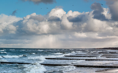 A snow storm in the distance, over the sea. In the foreground, breakwaters on the beach.