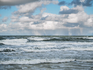 A snow storm in the distance, over the sea. In the foreground, strong waves near the shore on the beach.