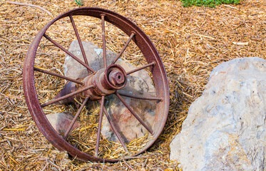a vintage rusted wagon wheel lying against a rock surrounded by straw