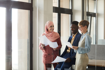 Waist up portrait of young multi-ethnic business team smiling happily and holding documents while...
