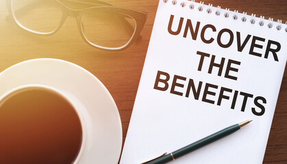 Uncover the Benefits - text written on notebook on wooden table with pen coffee and glasses