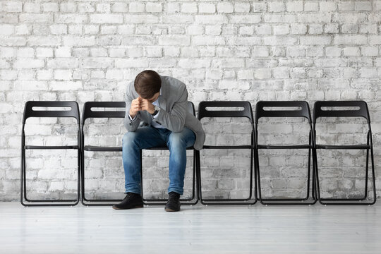 Desperate sad jobless man put head on hands sitting on chair hunched after unsuccessful failed job interview meeting. Fired employee feels stressed after dismissal, boss and company bankruptcy concept