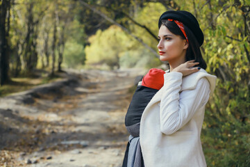 Beautiful young mother with her infant baby in sling outdoor. Woman is carrying her child and walk...