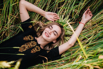A young, slender girl in embroidery lies in wheat ears in a field