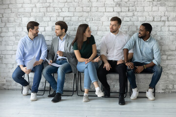 Involved in friendly conversation diverse people one girl multi ethnic guys sit on chairs in office hall wait for group meeting or seminar discuss work moments. Job interview applicants talk concept