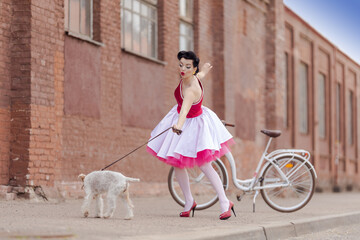 A girl in a dress and hairstyle in the style of the 40-50s on the city street with a dog breed Fox...