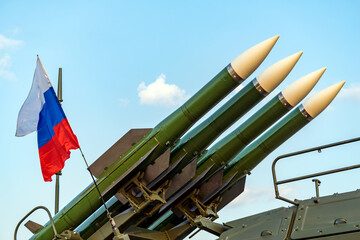 Ballistic missile launcher with four cruise missiles on powerful mobile transportation on background blue sky, antiaircraft forces, military industry. Flag of Russia