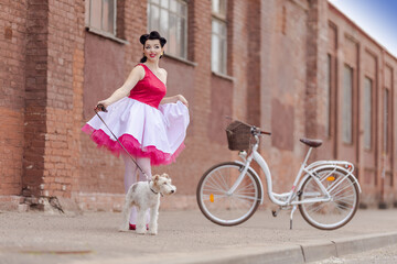 A girl in a dress and hairstyle in the style of the 40-50s on the city street with a dog breed Fox...