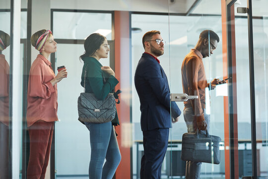 Side view at multi-ethnic group of business people standing in line in office behind glass wall, copy space