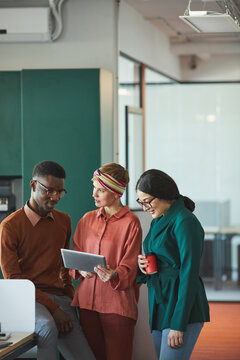 Vertical Portrait Of Three Contemporary Business People Discussing Work In Office, Focus On Young Woman Holding Tablet And Talking To Colleagues, Copy Space