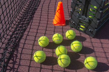 tennis ball on court by the net near the bucket to be picked-up. sunny day.