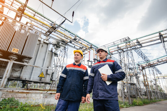 Two specialist electrical substation engineers inspect modern high-voltage equipment in the evening. Energy. Industry