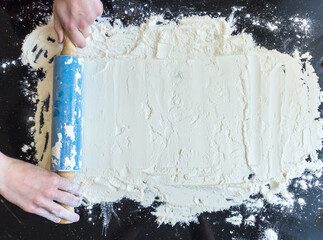 Rolling pin in woman hands and white flour on dark background.