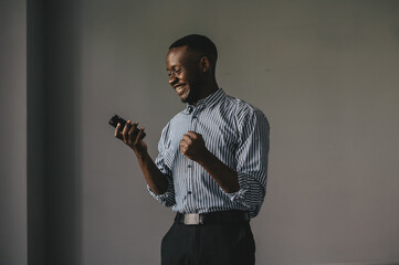 the African-American answered the phone and got some very good news. happy african guy euphoric looking at cell phone celebrate good news victory success