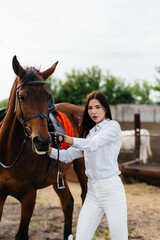 A young pretty girl rider poses near a thoroughbred stallion on a ranch. Horse riding, horse racing