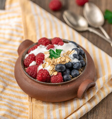 Granola with white yogurt with raspberries and blueberries in ceramic bowl on stripped napkin.