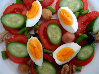A healthy Mediterranean diet plate with tomatoes, cucumbers, peppers, balck and green olives. walnuts and eggs.