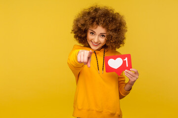 Internet blogging. Portrait of cheerful curly-haired woman in urban style hoodie pointing to camera...