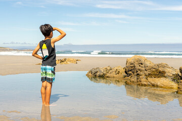 Child in the sand with his hand on his face to cover himself from the sun and to be able to observe...