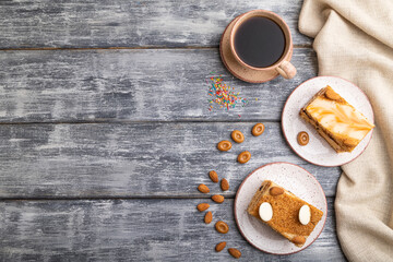 Honey cake with milk cream, caramel, almonds and a cup of coffee on a gray wooden background. Top view, copy space.