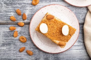 Honey cake with milk cream, caramel, almonds and a cup of coffee on a gray wooden background. Top view, close up.