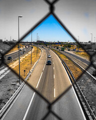 Colored highway with cars seen through a fence black and white. 