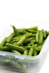 Garden peas in pods freshly picked in a plastic container,  isolated on a white background.  Grow your own concept