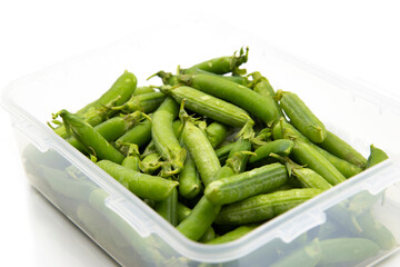 Garden peas in pods freshly picked in a plastic container,  isolated on a white background.  Grow your own concept