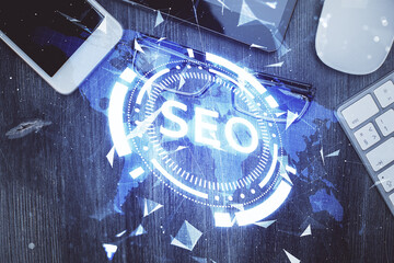 Double exposure of SEO hologram drawing over desktop. Top view. Search optimization concept.