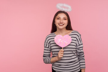 Happy Valentine's day! Angelic woman with holy nimbus holding pink paper heart and smiling to...