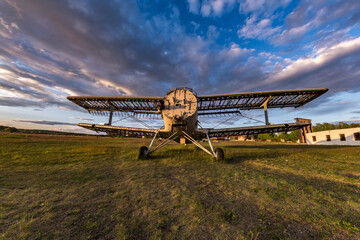 Old destroyed plane in the field in the rays of the setting sun with beautiful clouds