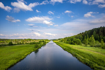 Fototapeta na wymiar landscape of a beautiful wide river or channel on a sunny day with blue reflection with beautiful clouds in the water