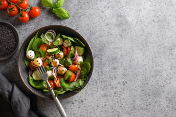 Salad with spinach, cherry tomatoes, onion and Mozzarella on grey stone background. Top view.