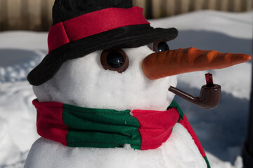 Close up of snowman with carrot nose and pipe with felt hat and scarf after a fresh snowfall.