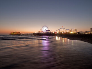 Dusk view of popular Santa Monica pier reflecting in pacific ocean water in Southern California.