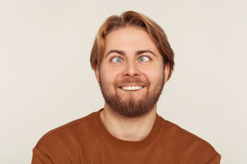 Closeup portrait of idiot, dumb bearded man looking cross-eyed with stupid smile, fooling around, making silly face, brainless comical expression. indoor studio shot isolated on gray background - obrazy, fototapety, plakaty