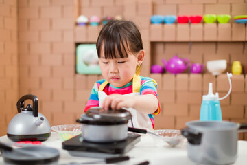 toddler girl pretend play food preparing role against cardboard blocks kitchen background